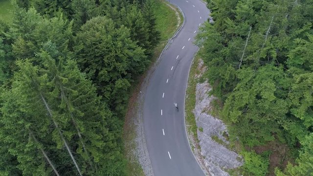 Aerial - Man skateboarding on a road through the forest with car driving by