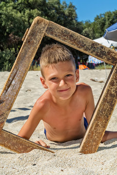 Pretty boy on beach with wooden picture frame