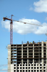 Big hoisting tower crane and top section of modern construction building in a city over blue sky with white clouds