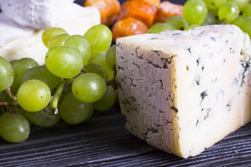Cheese cuts with figs, nuts, honey, grapes on a dark rustic wooden boards background