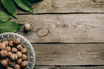 top view of tasty healthy walnuts on plate and green leaves on wooden table