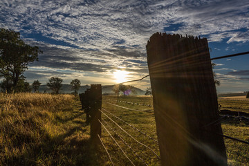 Sun shining through country fence line with cloudy sky