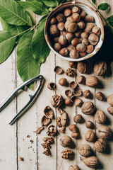 top view of delicious cracked walnuts, hazelnuts, green leaves and nutcracker on wooden table