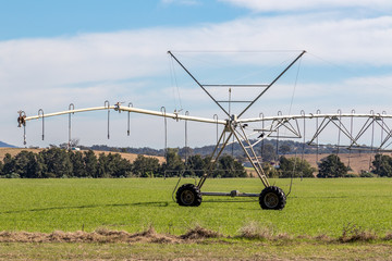 Travelling irrigator on farmland against cloudy blue sky