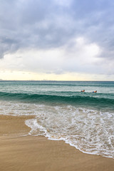 Surfers waiting to catch a wave against ocean and cloudy sky