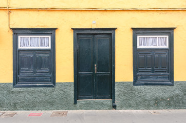 green door and two windows on a yellow facade of an old house