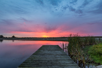 Colourful sunrise over timber jetty and lake