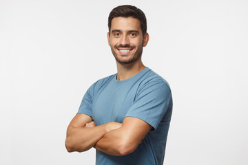 Smiling handsome young man in blue t-shirt standing with crossed arms, isolated on grey background