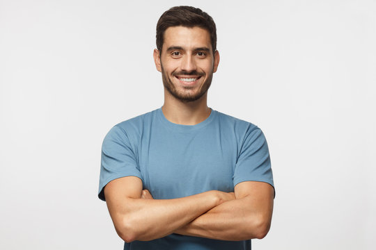 Portrait of smiling handsome man in blue t-shirt standing with crossed arms isolated on grey background