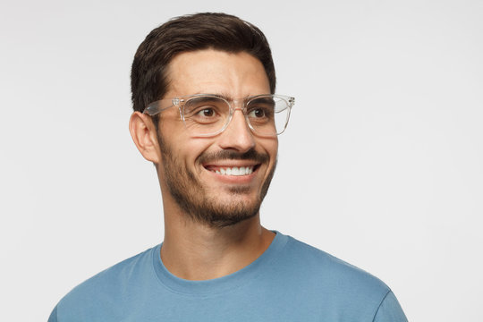 Close Up Portrait Of Smiling Handsome Male In Blue T-shirt And Transparent Eyeglasses Looking Right, Isolated On Gray Background