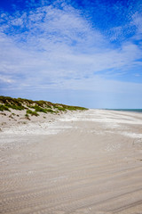 White sandy beach below cloudy blue sky