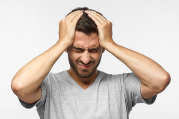 Headache concept. Upset unhappy young man squeezing head with hands. People, stress, tension and...