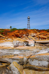 Lighthouse tower against rocky coastline and blue sky 