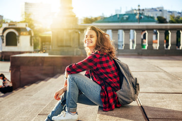 Beautiful young happy smiling woman against the background of a European city in the sun at sunset, student and traveler, vacation in the city