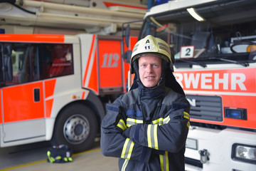 Fototapeta premium Beruf Feuerwehrmann - Portrait in der Feuerwache vor Feuerwehrfahrzeugen im Depot - Rettungsdienst 112 // firemen in the fire station in front of fire engines in the depot - rescue service 