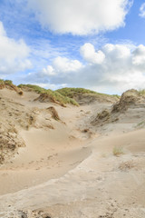Dune valleys with deep wind holes carved out by heavy storm with swaying marram grasses with scattered clouds against blue sky