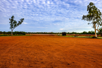 Red dirt landscape against trees and cloudy blue sky