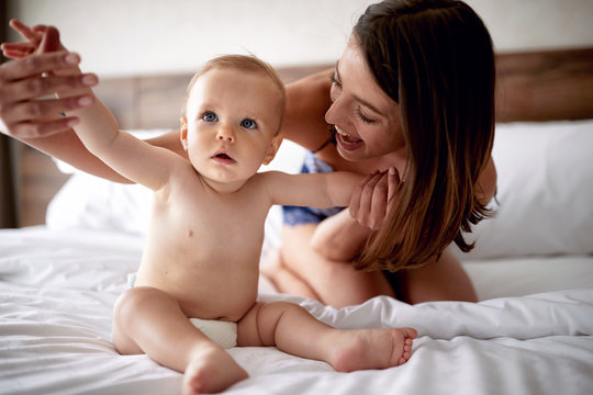 Mother And Baby In Bed. Young Mom Playing With Her Son. Child And Parent Together At Home. Happiness And Motherhood.