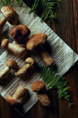 top view of fresh picked boletus edulis mushrooms on newspaper and fern on wooden table