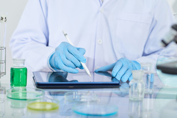 Fototapeta premium Close-up of chemist in protective glove using digital tablet in his work at lab
