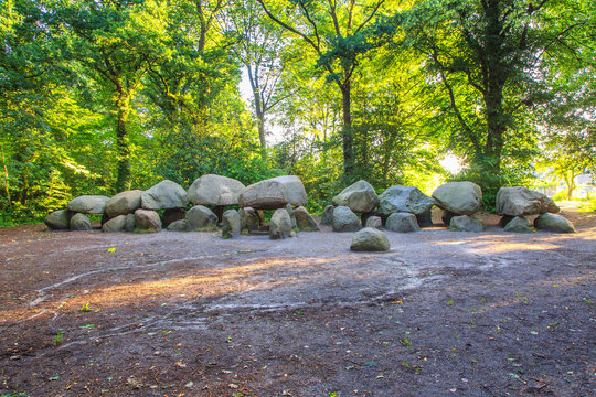 Dolmen D27 in the Dutch province of Drenthe with a background of oak trees and lights of the rising sun . A dolmen is construction work from the new stone age