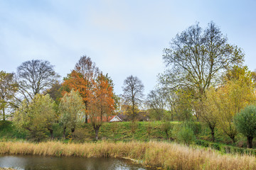 Obraz premium Fort Everdingen part of the Nieuwe Hollandse Waterlinie behind earthen fortification wall covered with trees in autumn colours and fort Canal in the foreground