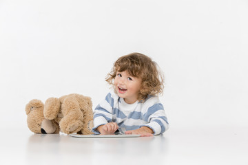 Portrait of happy joyful beautiful little boy sitting with laptop and teddy bear toy , studio shot on white