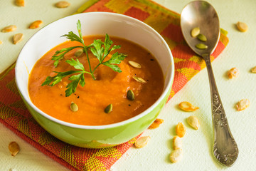 Autumnal orange color pumpkin soup with parsley in the green bowl on an orange color cloth napkin