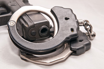 A pair of black and silver handcuffs draped over a black pistol muzzle on a white background