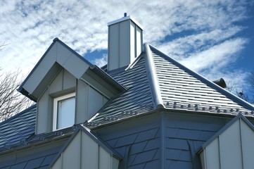 Frisch renoviertes, mit grauen Metallschindeln gedecktes Haus mit Aufkeilfenstern/Gaubenfenstern und Schornstein mit Stehfalz-Metallverkleidung und Schneefang, regenfallrohr und Dachrinne
