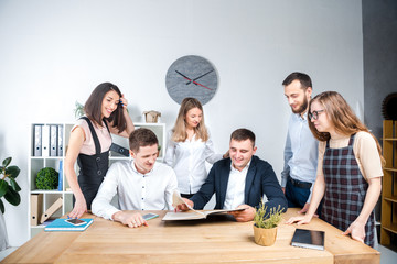 Theme is business and teamwork. A group of young Caucasian people office workers holding a meeting, briefing, working with papers and documents in a light office office around a wooden table