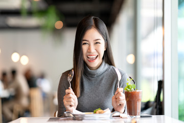 Young attractive asian woman holding fork and spoon feeling hungry, excited, happy and ready to eat...