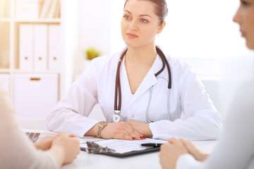 Brunette female doctor talking to patient at hospital office. Physician says about medical exams results for choosing optimal treatment. Healthcare and medicine concept