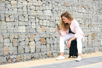 Woman sitting on the luggage and using smart phone.