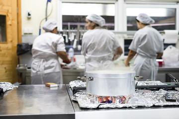 Steaming silver pot with three kitchen workers in restaurant