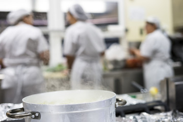 Steaming silver pot with three kitchen workers in restaurant