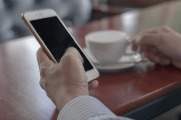 Closeup image of businessmen hands holding mobile with blank copy space screen for your text message or promotional content against desktop and cup of cool tea.