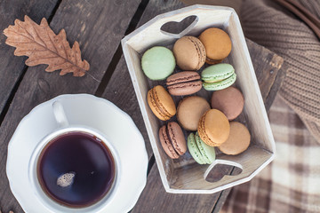 A cup of hot tea, macaroons, a knitted sweater on a wooden table. Autumn. Winter. Cozy.