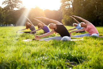 Mixed age group of people practicing yoga outside in the park while sunset - obrazy, fototapety, plakaty