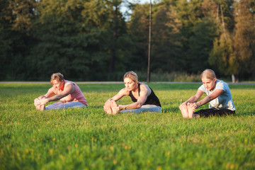 Fototapeta premium Yoga at park, group of mixed age women doing pose while sunset