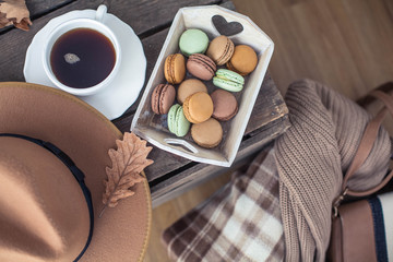 A cup of hot tea, macaroons, a knitted sweater, a hat, a rug on a wooden table. Autumn. Winter. Cozy.