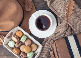 A cup of hot tea, macaroons, a knitted sweater, a hat, a rug on a wooden table. Autumn. Winter. Cozy.