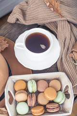 A cup of hot tea, macaroons, a knitted sweater, a hat, a rug on a wooden table. Autumn. Winter. Cozy.