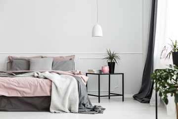 Warm blankets and gray pillows on a cozy double bed with dirty pink sheets by an empty wall of a white bedroom interior