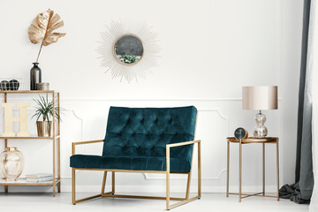 Golden decorations and furniture in an expensive living room interior with an emerald green sofa by a white wall with molding