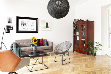 Black lamp above armchair and table in bright living room interior with poster and plants. Real...