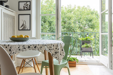 Real photo of a scandi dining room interior with a patterned cloth on a table, chairs and balcony...