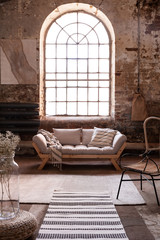 Fototapeta na wymiar Window above grey wooden settee in spacious living room interior with armchair and rug. Real photo