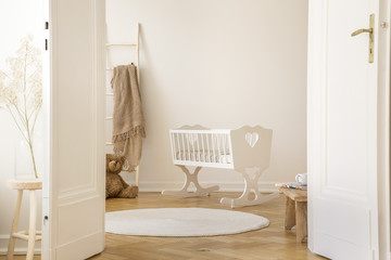 Real photo of white cradle with heart standing in Scandi kid room interior with teddy bear,...
