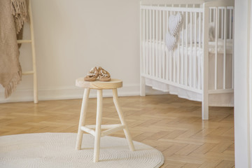 Real photo of little baby shoes placed on wooden stool standing in white kid room interior with...